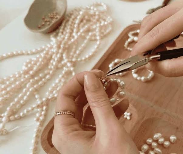 Hands stringing pearls into a necklace on a bead design board